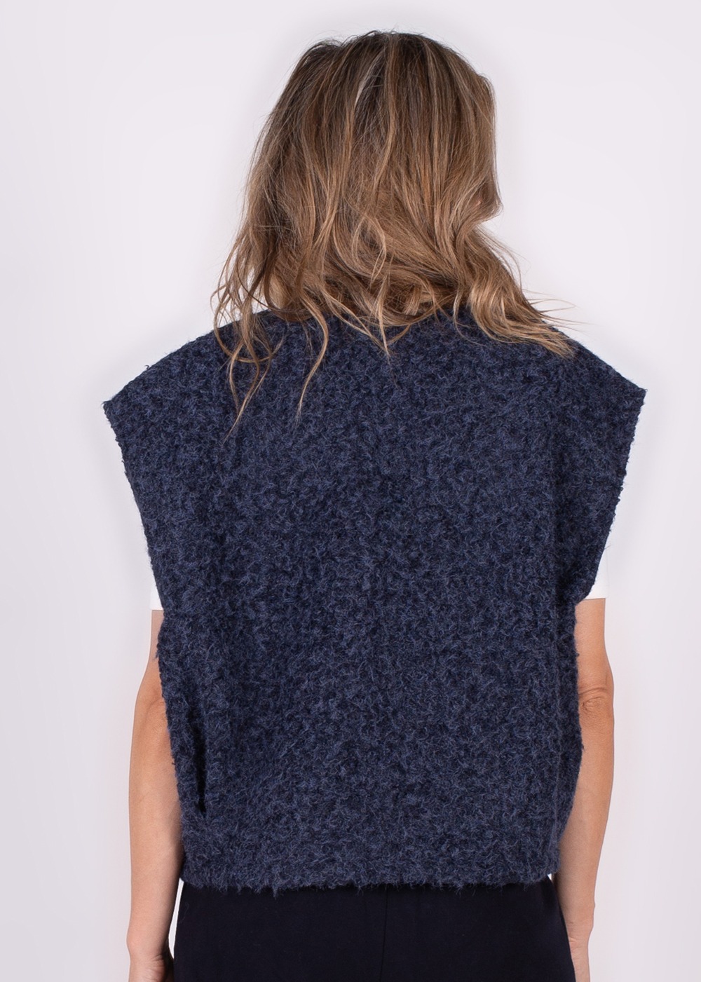 Achteraanzicht van een persoon met halflang haar die een donkerblauw, wollig Matsumoto gilet draagt.
