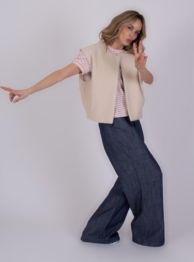 Vrouw poseert in een Matsumoto teddy bodywarmer, roze gestreept T-shirt en wijde donkerblauwe broek.