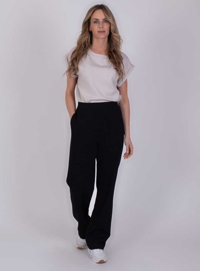 Vrouw draagt een witte top en zwarte Mesuru black broek met wijde pijpen en witte sneakers.