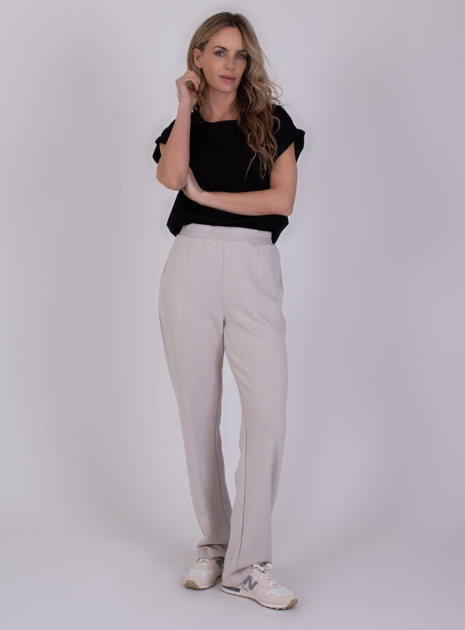 Vrouw draagt de Mesuru kit 2 outfit met een zwarte top en beige broek met sneakers.