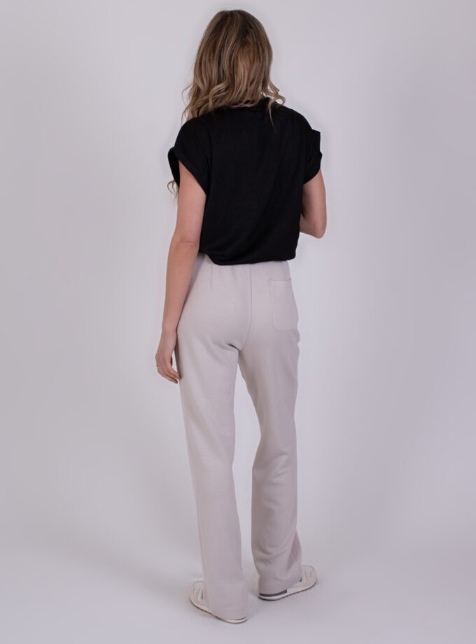 Vrouw draagt de Mesuru kit 5 outfit met een zwarte top en beige broek, gefotografeerd van achteren tegen een neutrale achtergrond.