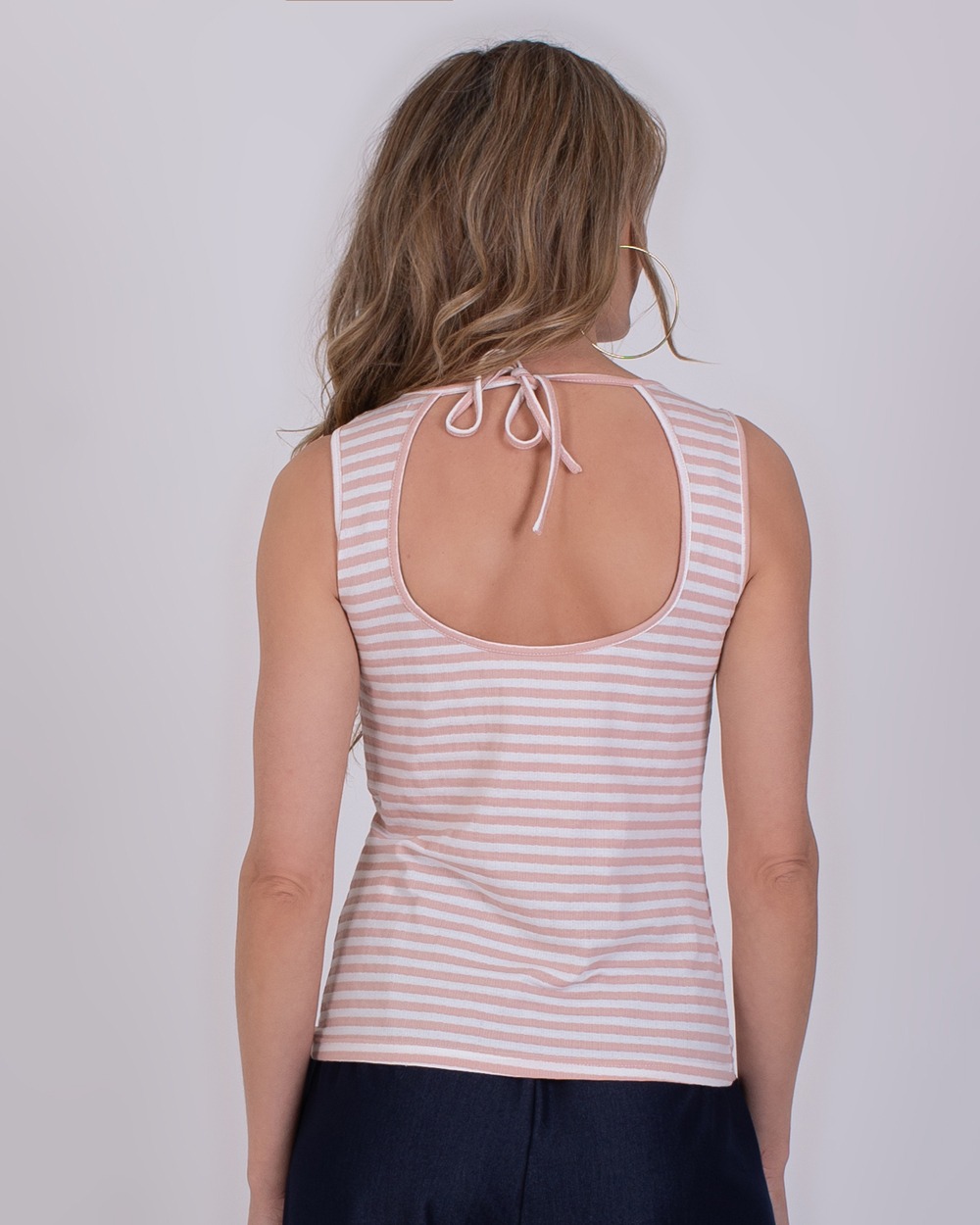 Namur old pink-offwhite 5 Vrouw met lang haar draagt een mouwloze, roze-wit gestreepte Namur top met open rug en striksluiting.