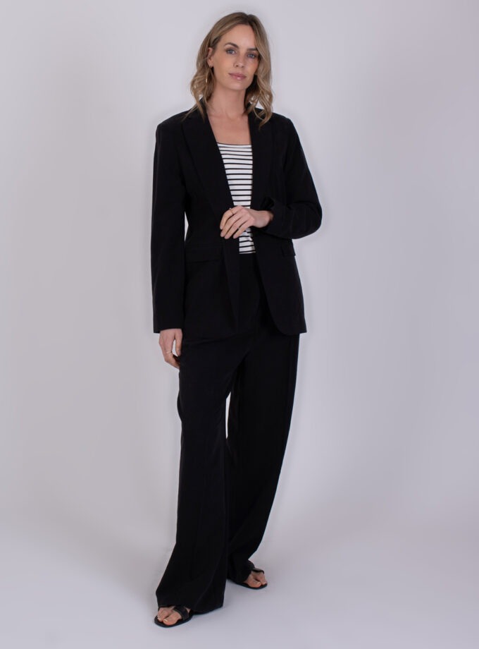 Vrouw draagt een zwarte Opole broekpak met een zwart-wit gestreepte top en zwarte sandalen.