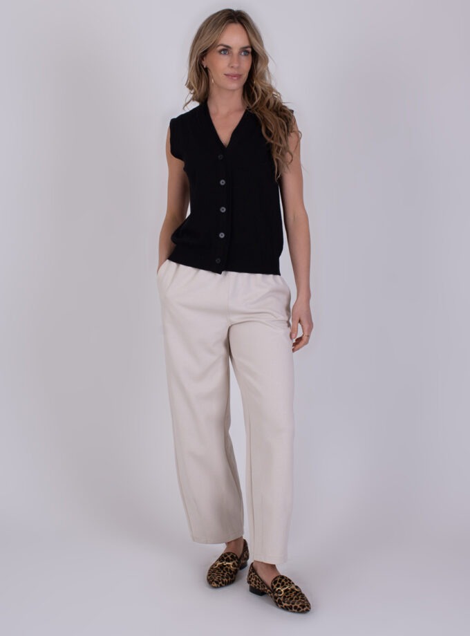 Vrouw draagt een mouwloze zwarte Patras black 2-top met knopen, beige broek en panterprint loafers.