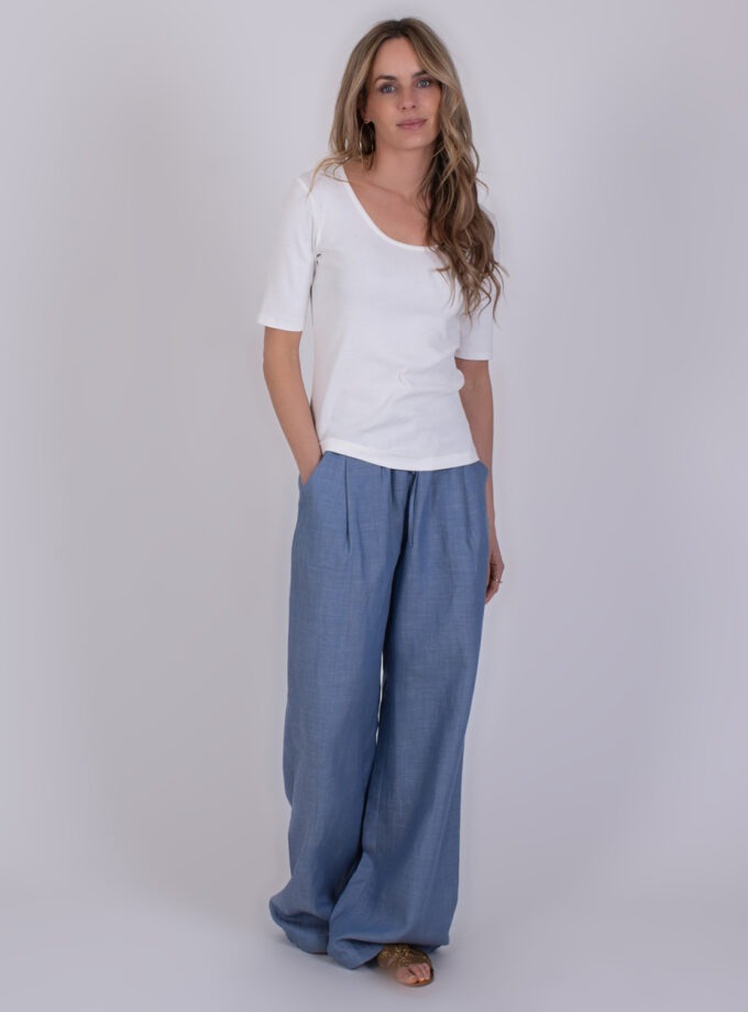 Vrouw draagt een offwhite Perm-top met halve mouwen en losse, lichtblauwe broek.