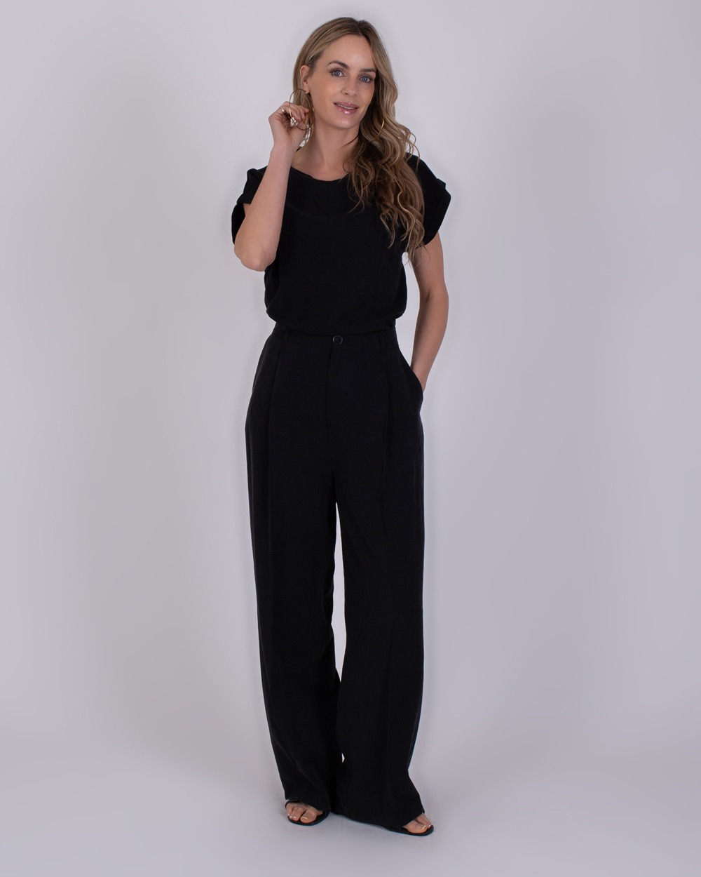 Piran black 1 Vrouw draagt een zwarte Piran jumpsuit met korte mouwen en wijde pijpen.