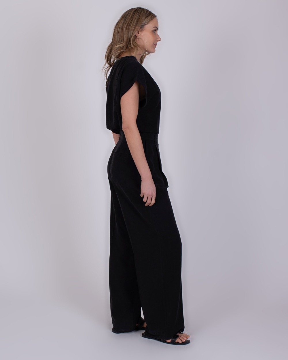 Piran black 3 Vrouw in zijaanzicht draagt een zwarte Piran jumpsuit met wijde pijpen en korte mouwen.