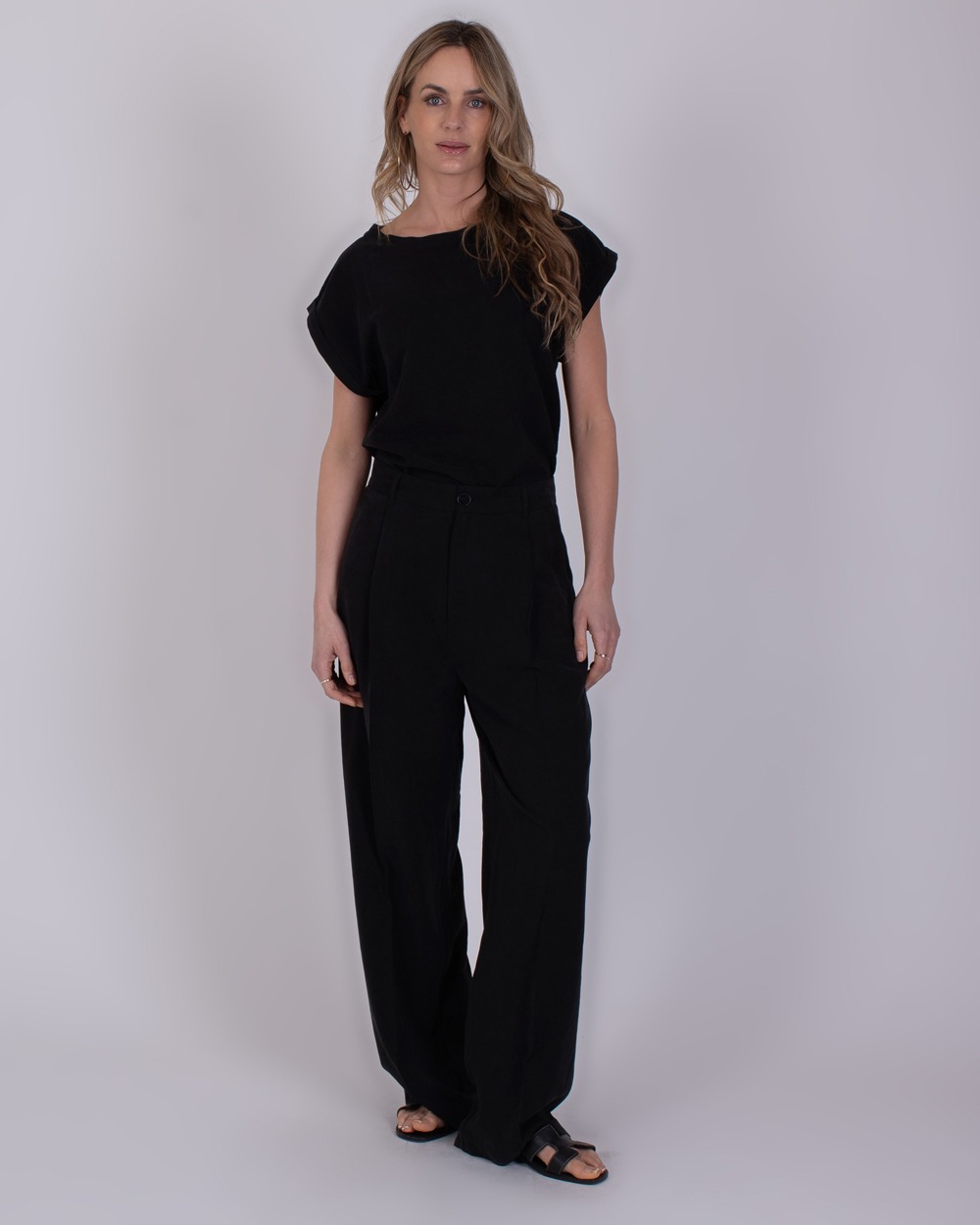 Piran black 5 Vrouw draagt een zwarte Piran black 5 outfit met wijde broek en sandalen tegen een neutrale achtergrond.