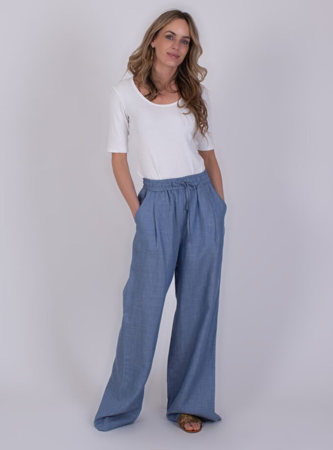 Vrouw draagt een witte top en wijde Pune light jeans blauwe broek met elastische tailleband.
