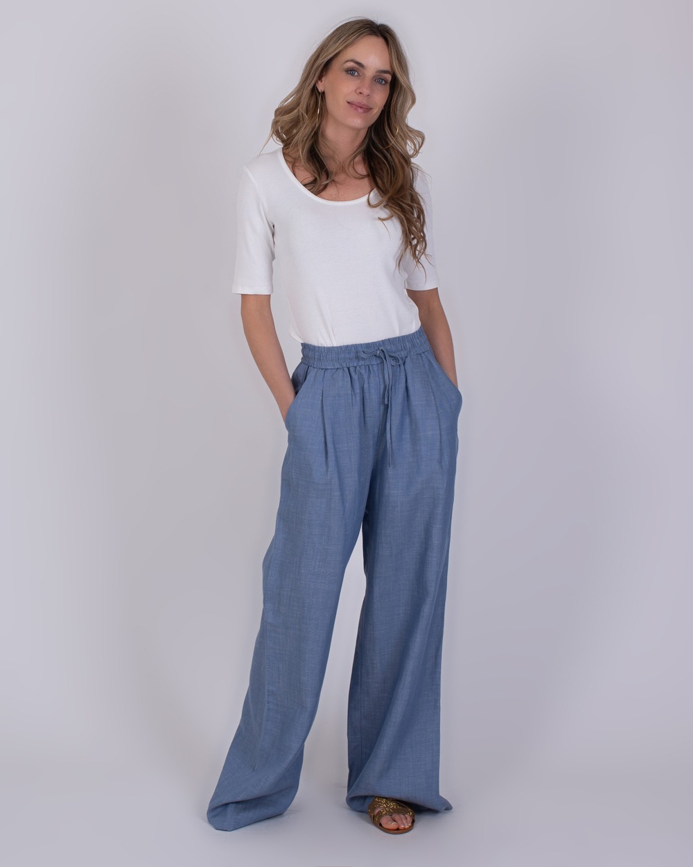Vrouw draagt een witte top en wijde Pune light jeans blauwe broek met elastische tailleband.