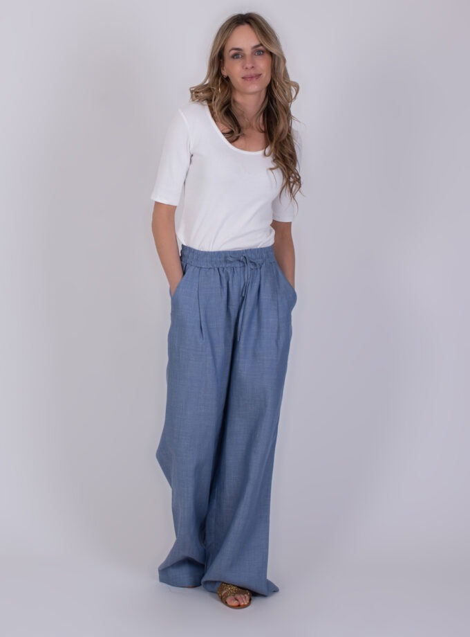 Vrouw draagt een witte top en wijde Pune light jeans blauwe broek met elastische tailleband.