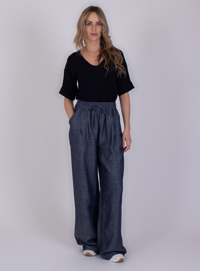 Vrouw draagt een zwarte top en een wijde, mediumblauwe Pune-broek met elastische tailleband.