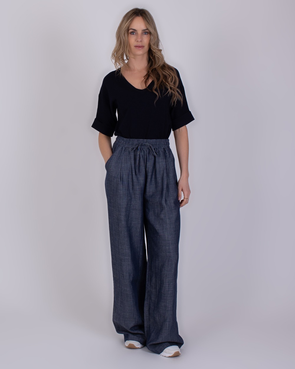 Pune medium blue 1 Vrouw draagt een zwarte top en een wijde, mediumblauwe Pune-broek met elastische tailleband.