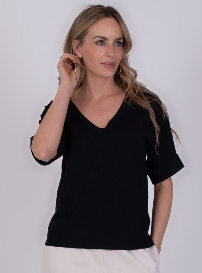 Vrouw draagt een zwarte Pylos trui met V-hals en opgerolde mouwen.