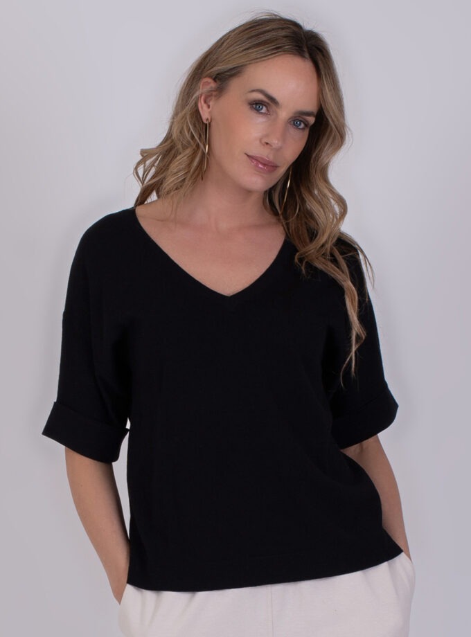 Vrouw draagt een zwarte Pylos black 2 top met V-hals en opgerolde mouwen.