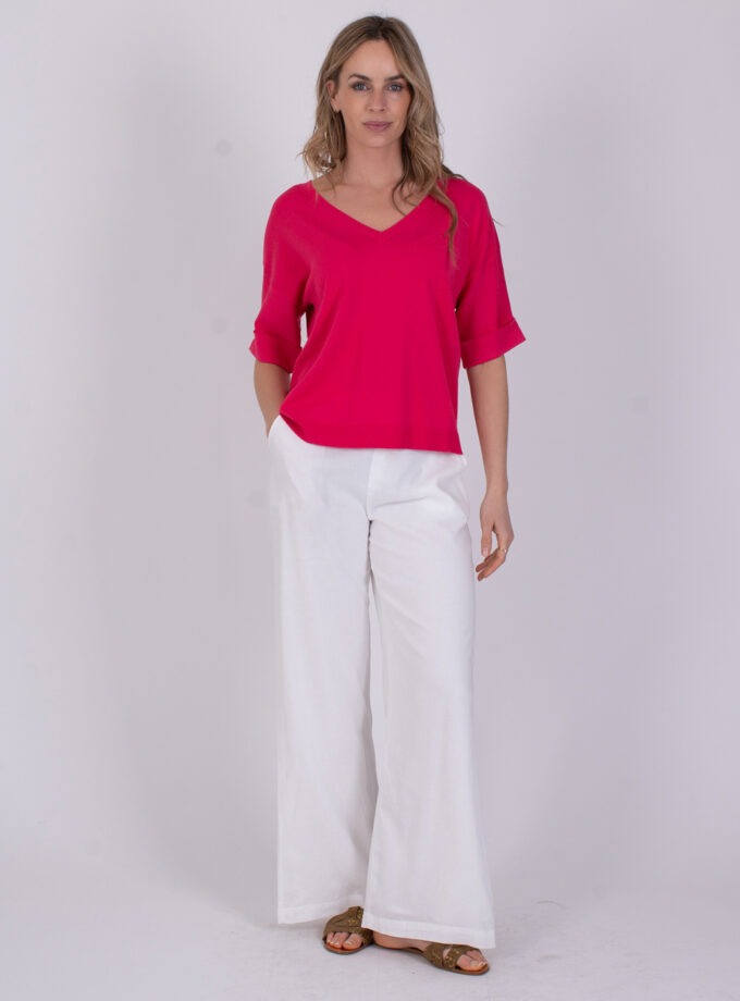 Vrouw draagt een fuchsia Pylos-top met V-hals en witte, wijde broek.