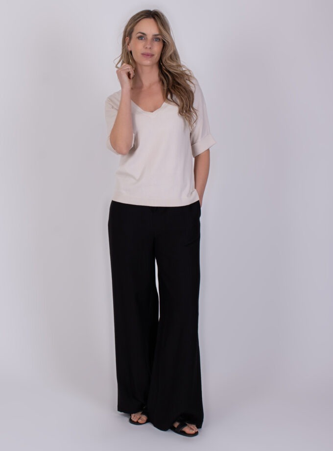 Vrouw draagt de Pylos kit 1 met een lichtbeige top en zwarte, wijde broek.