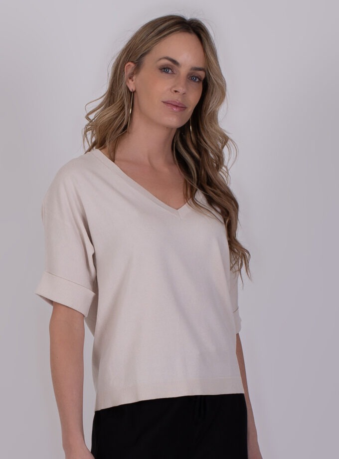 Vrouw draagt een lichtbeige Pylos Kit 3 trui met V-hals en opgerolde mouwen.