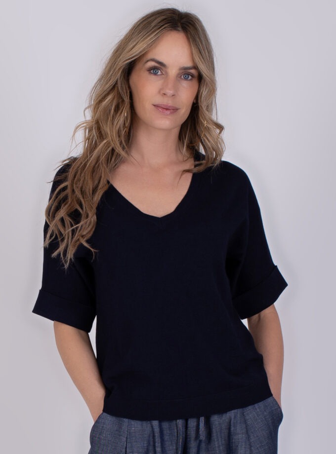 Vrouw draagt een navykleurige Pylos trui met V-hals en opgerolde mouwen.