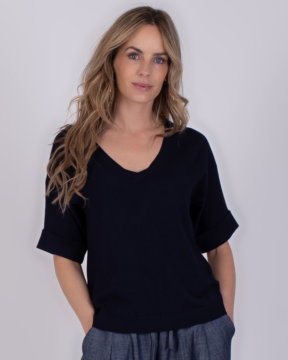 Vrouw draagt een navykleurige Pylos trui met V-hals en opgerolde mouwen.