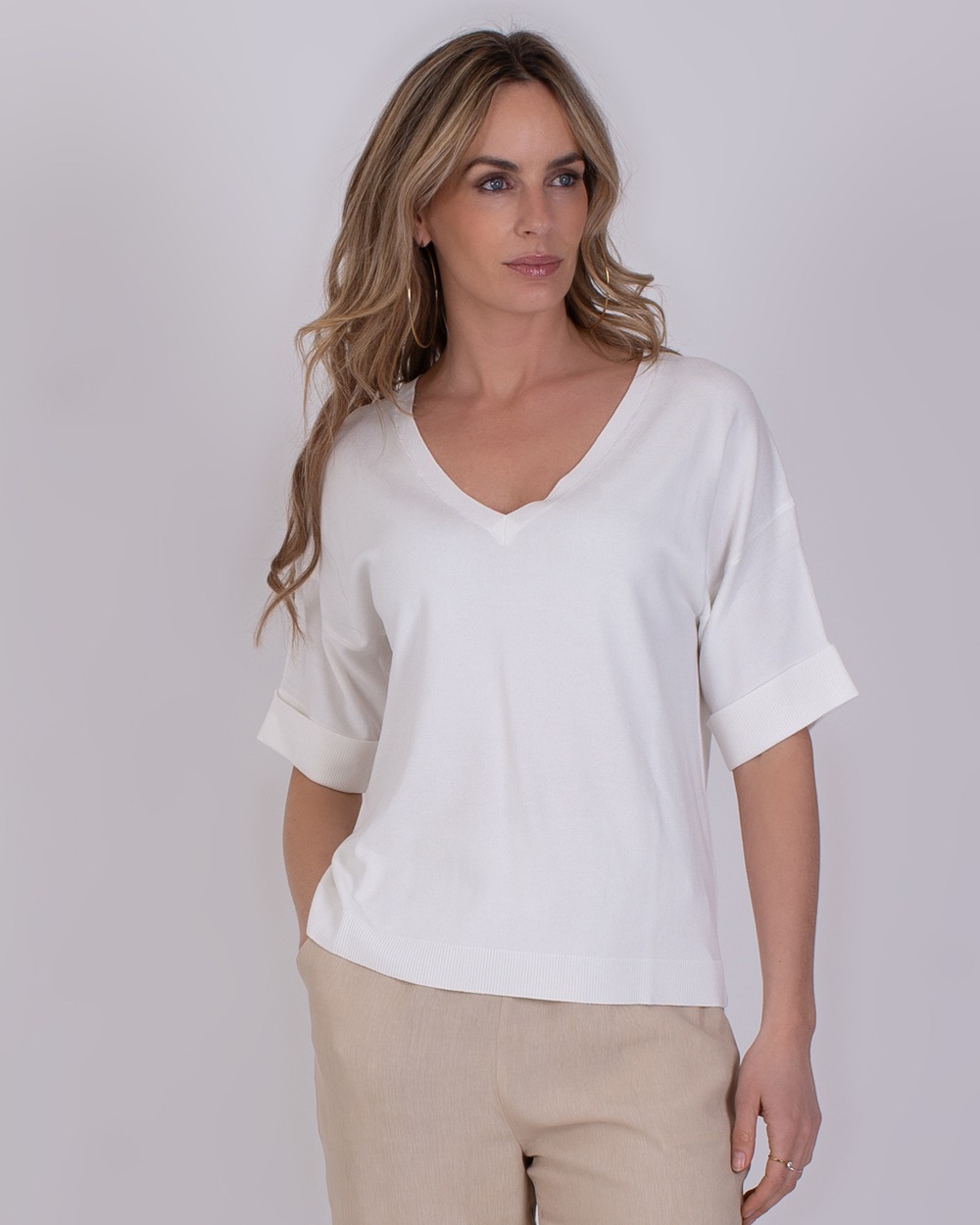 Vrouw draagt de Pylos off white top met V-hals en opgerolde korte mouwen.