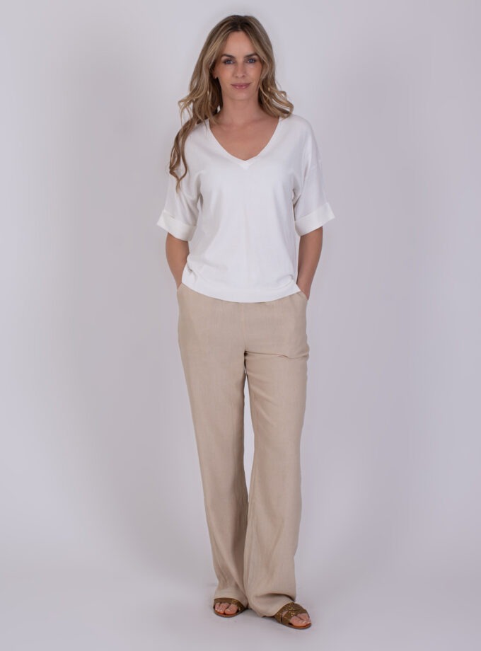 Vrouw draagt de Pylos off white top met een V-hals en beige linnen broek.