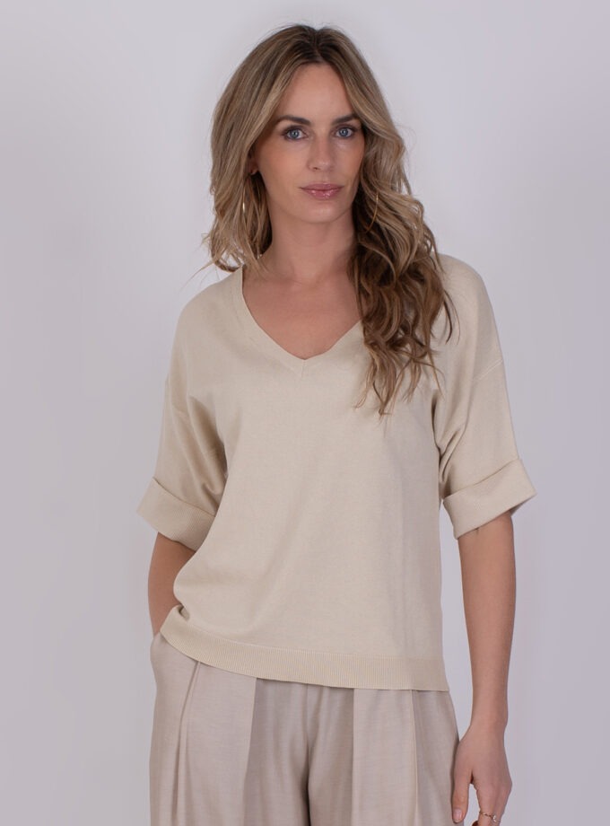 Vrouw draagt een beige Pylos Pale 1 trui met korte mouwen en geplooide beige broek.