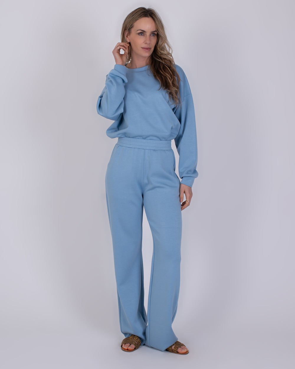 Rimini soft blue 3 Vrouw draagt een lichtblauwe Rimini soft blue lounge-set met lange mouwen en wijde broekspijpen.