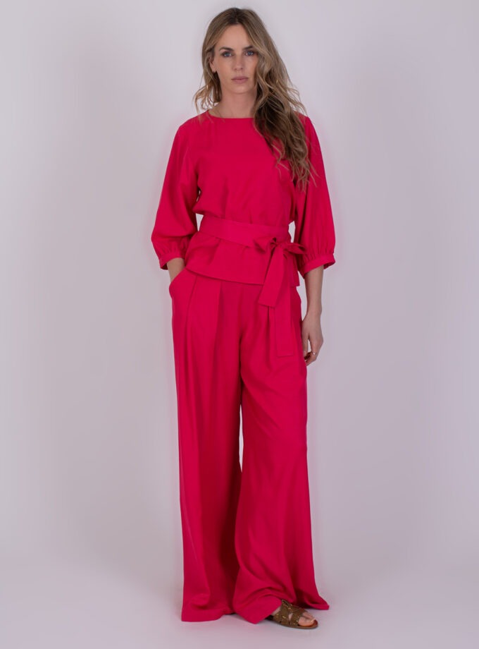 Vrouw draagt een fel fuchsia Riyad-pak met wijde broek en strikceintuur.
