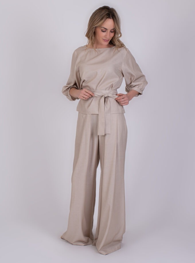 Vrouw draagt een lichtbeige Riyad Pale 2-set met wijde broek en top met strikceintuur.