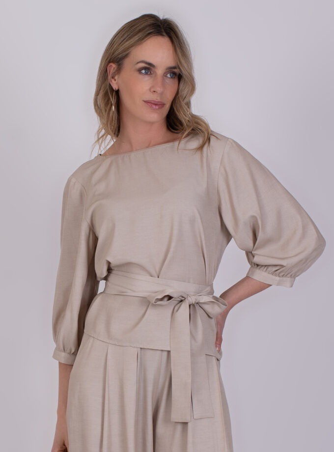 Vrouw draagt een elegante, beige Riyad pale 4-set met pofmouwen en strikceintuur.