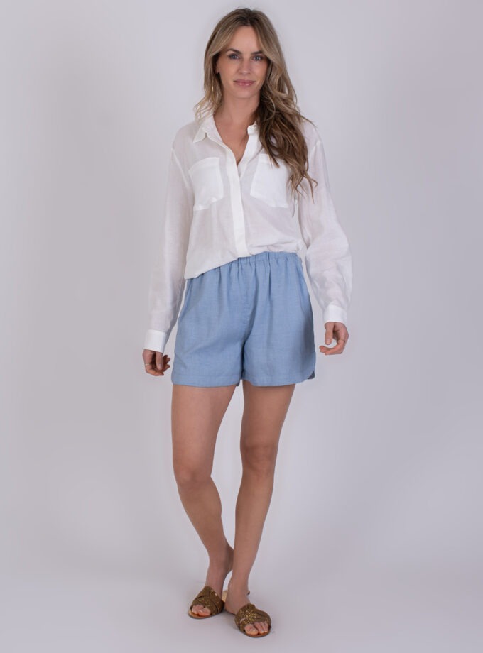 Vrouw draagt een off white blouse 'Seoel' met lange mouwen en lichtblauwe shorts.
