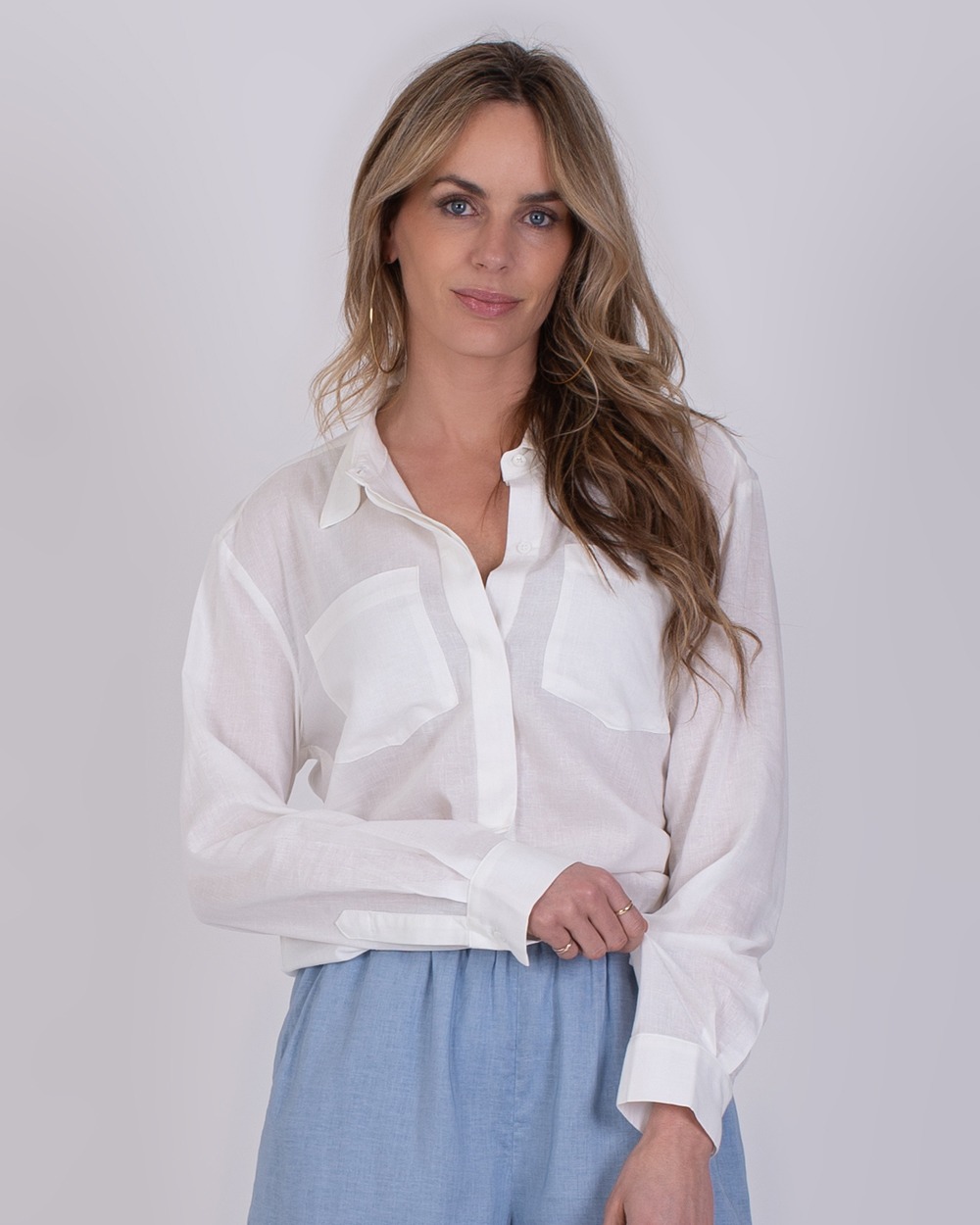 Vrouw draagt een lichte Seoel off white blouse met lange mouwen en lichtblauwe broek.