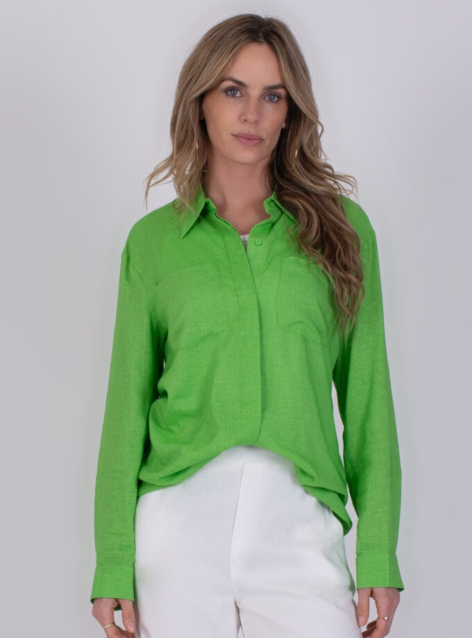 Vrouw draagt een felgroene Seoel Sea Green-blouse met lange mouwen en witte broek.