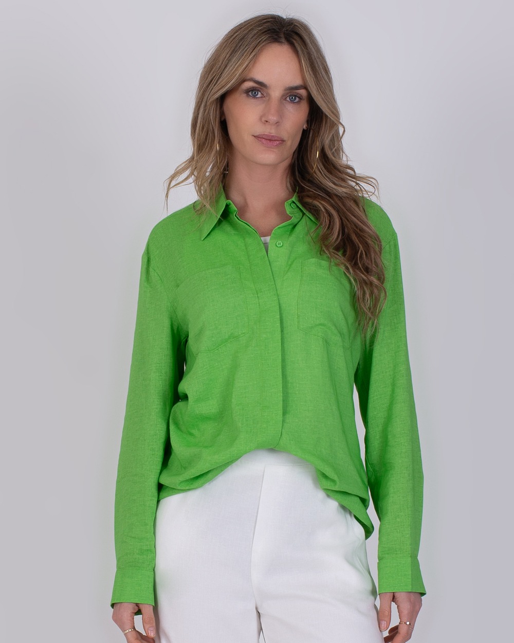 Vrouw draagt een felgroene Seoel Sea Green-blouse met lange mouwen en witte broek.