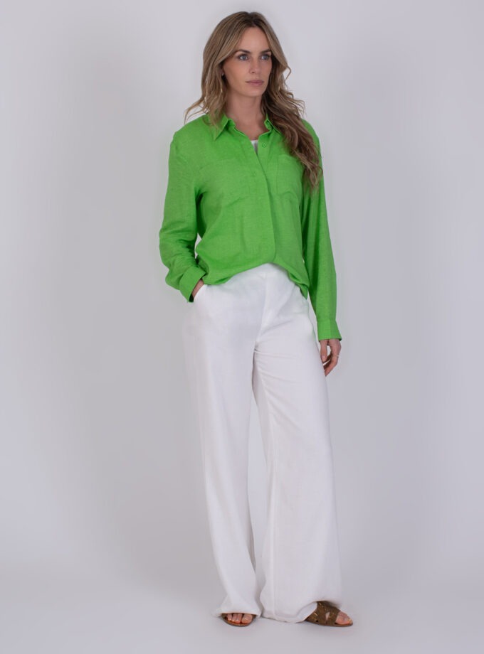Vrouw draagt een felgroene Seoel Sea Green blouse met witte, wijde broek en sandalen.