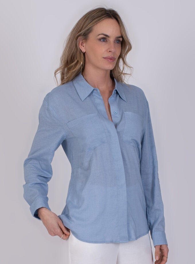Vrouw draagt een lichtblauwe blouse genaamd Seoel soft blue met lange mouwen en borstzakken.