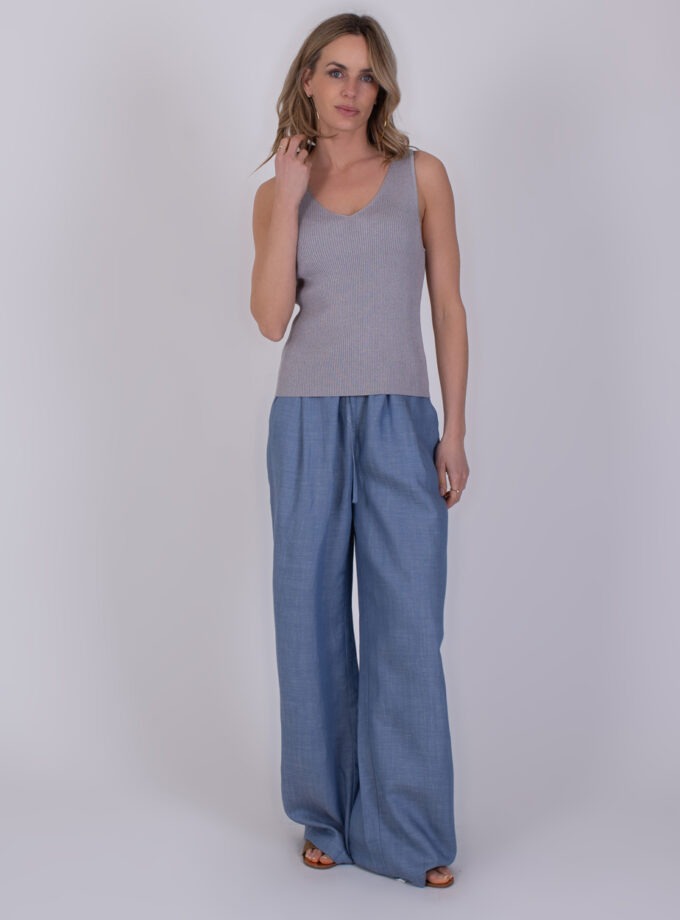 Vrouw in grijze Serres-top met V-hals en wijde lichtblauwe broek poseert tegen een neutrale achtergrond.