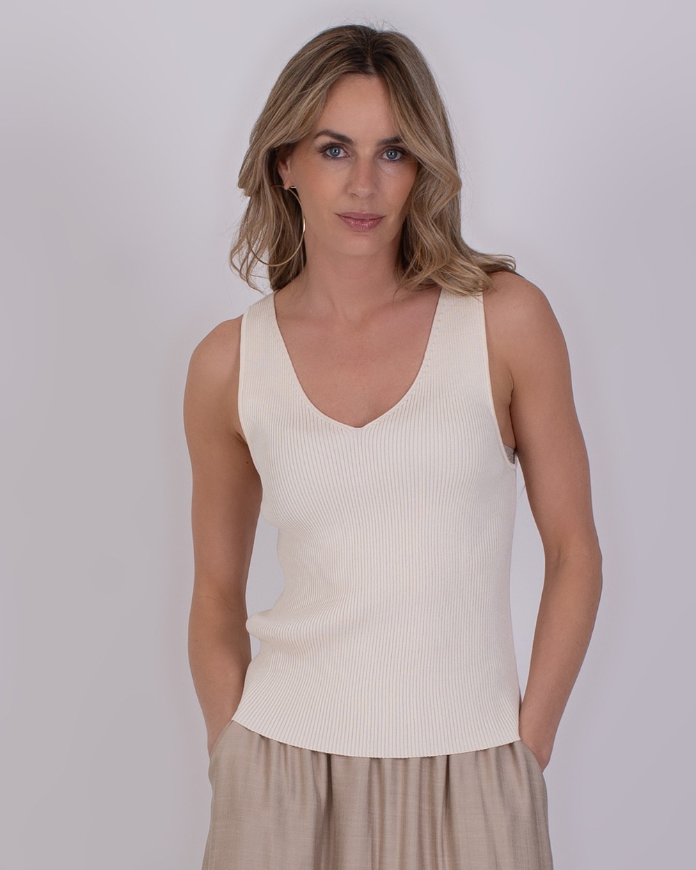 Serres pale 1 Vrouw draagt een mouwloze, geribde top in de kleur Serres Pale met een V-hals.