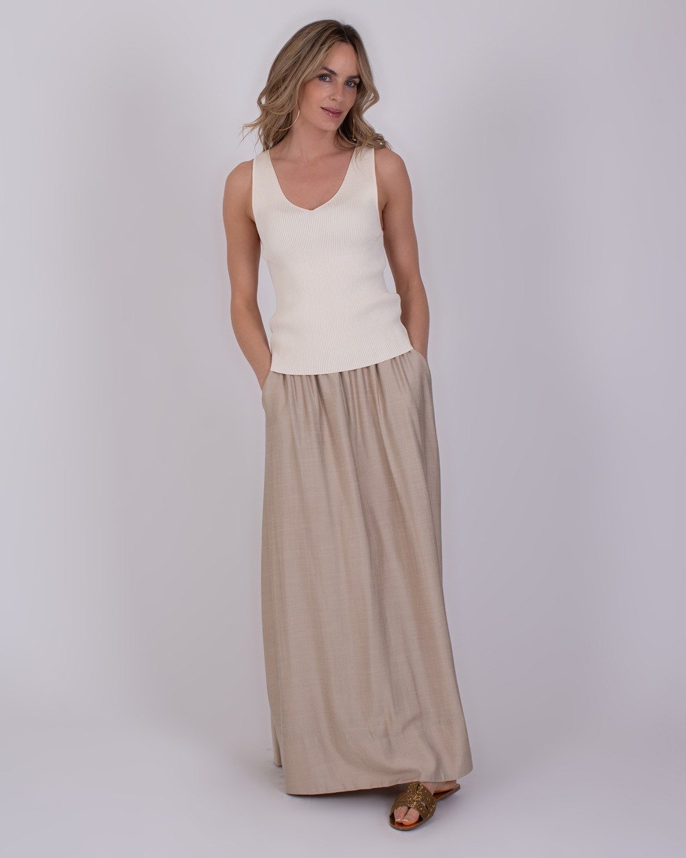 Serres pale 4 Vrouw draagt de Serres Pale 4 outfit met een gebroken witte top en een lange, beige rok.