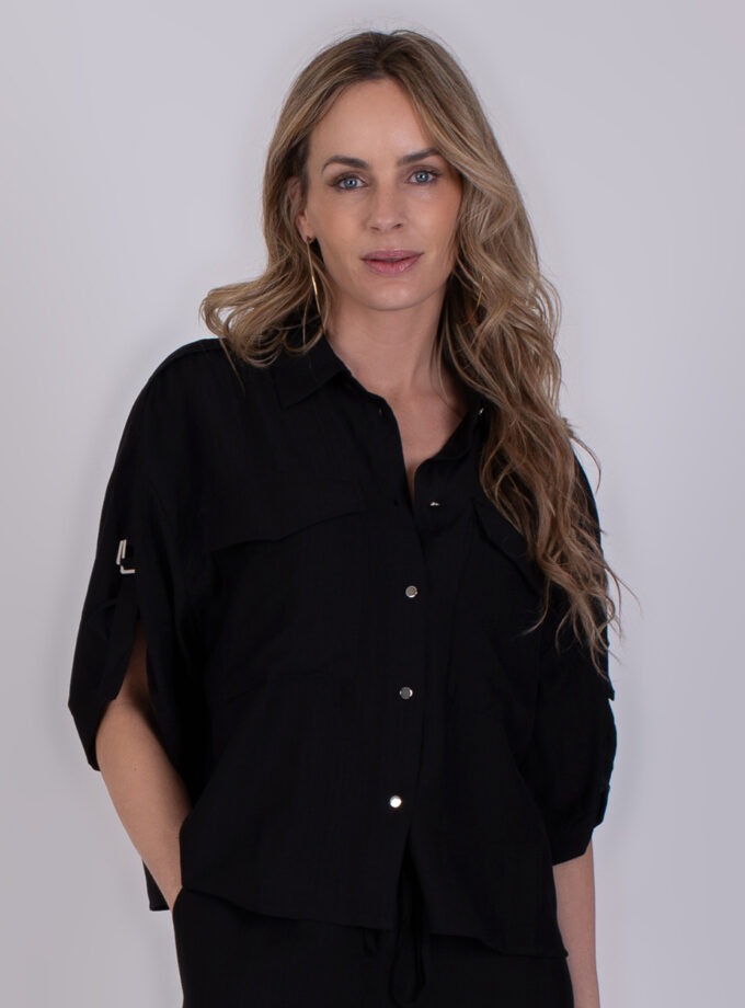 Vrouw draagt een zwarte Soppron-blouse met opgerolde mouwen en knoopsluiting.