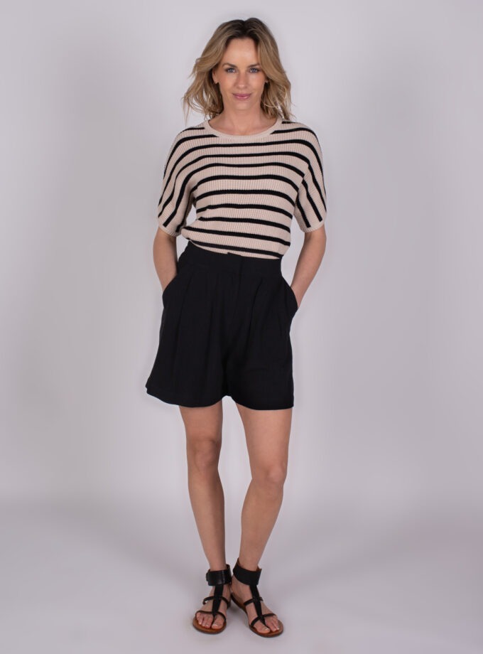 Vrouw in gestreepte trui en zwarte short poseert in studio voor Studio SS25 collectie.