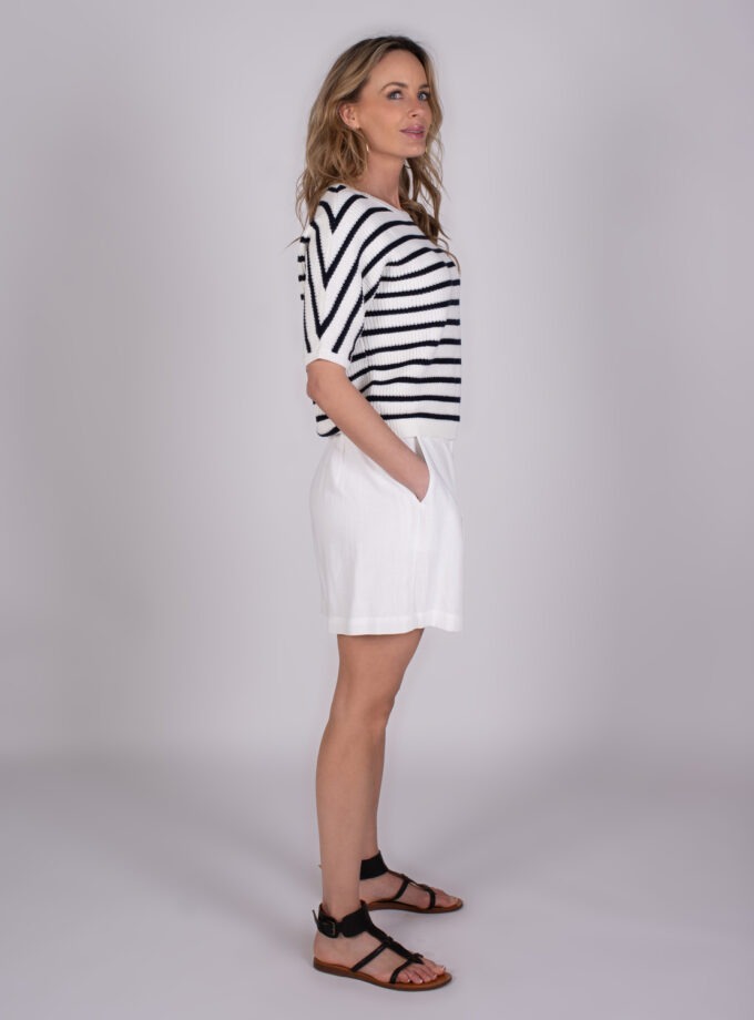 Vrouw in zijaanzicht draagt een zwart-wit gestreepte top met korte mouwen, een witte short en zwarte sandalen.