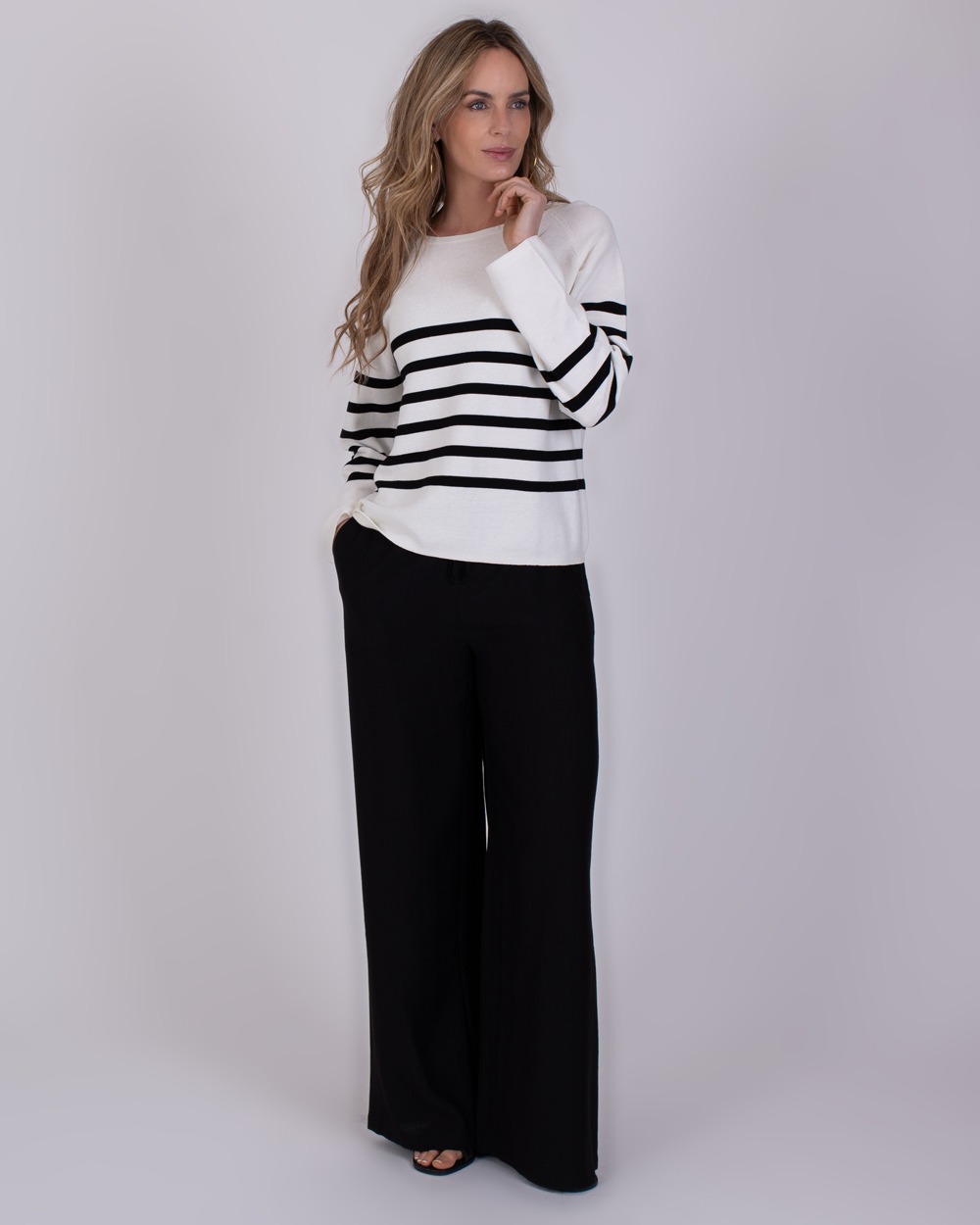 Trikala 1 Vrouw draagt een zwart-wit gestreepte trui en wijde zwarte broek uit de Trikala 1 collectie.