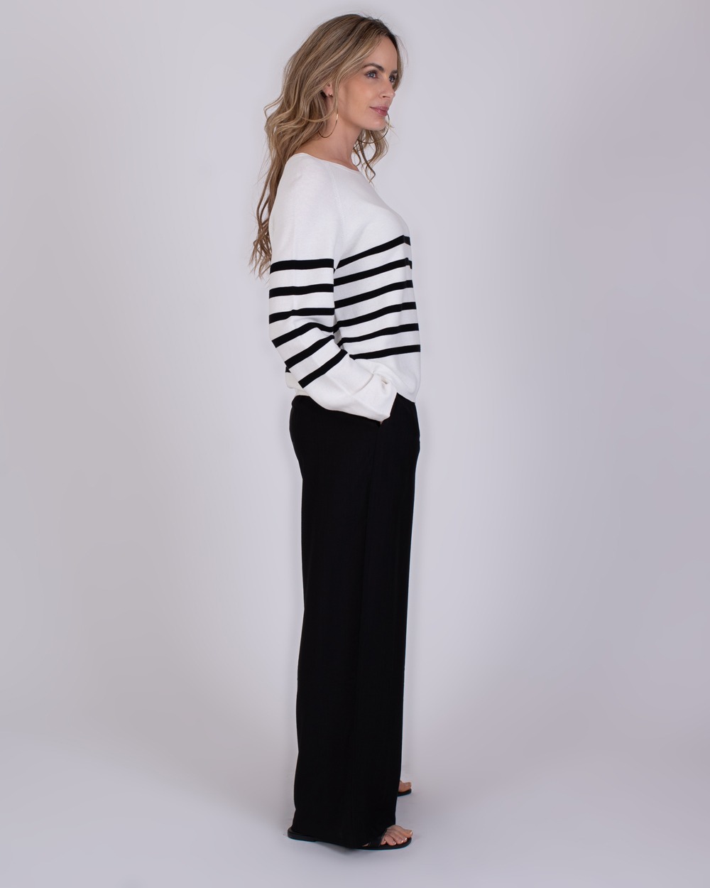 Trikala 2 Vrouw in zijaanzicht draagt de Trikala 2 trui met zwarte strepen en een zwarte broek.