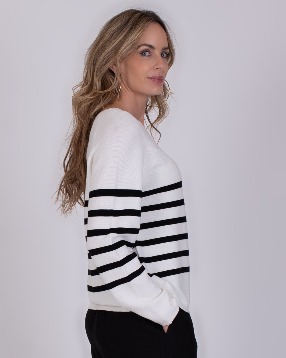 Trikala 4 Vrouw draagt de witte Trikala 4 trui met zwarte horizontale strepen en kijkt over haar schouder.