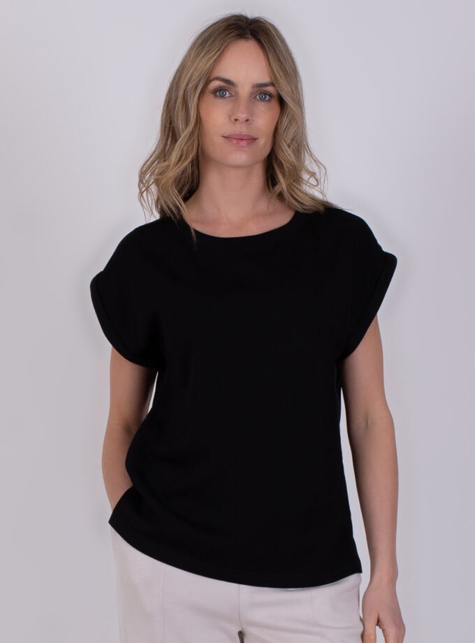 Vrouw draagt een zwarte Troje-top met opgerolde mouwen en een ronde hals.