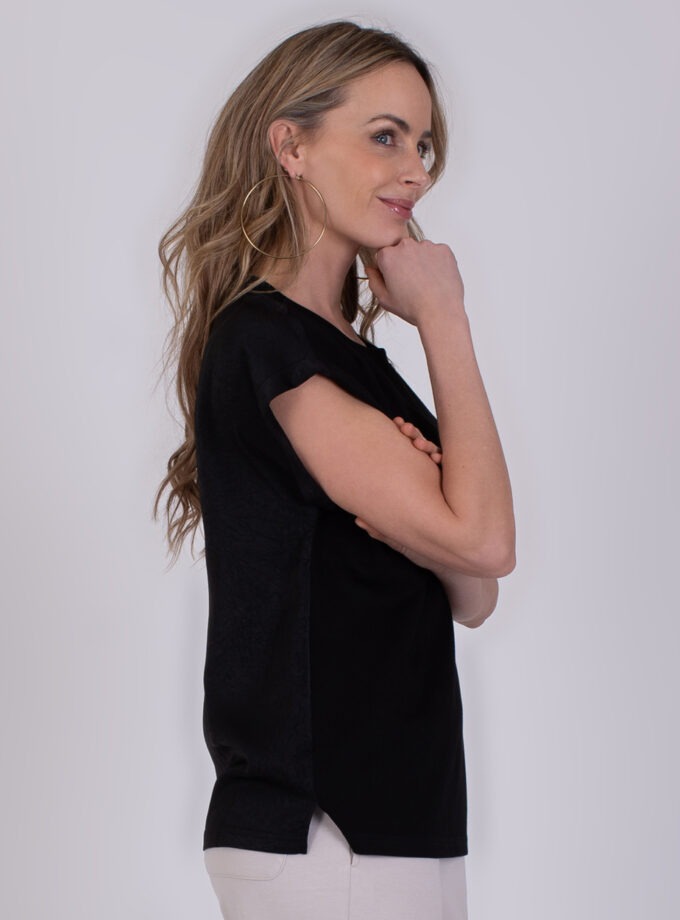 Vrouw in profiel poseert met de hand tegen haar kin terwijl ze een zwarte Troje-top draagt.