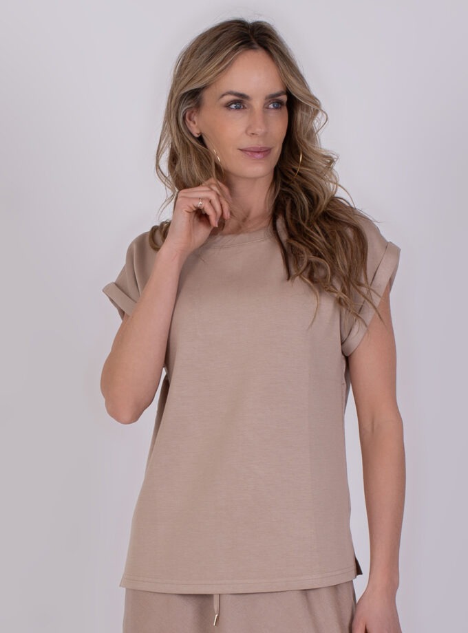 Vrouw draagt een beige top met opgerolde mouwen uit de Troje Pale 3 collectie.
