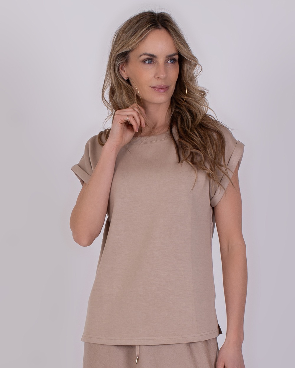 Vrouw draagt een beige top met opgerolde mouwen uit de Troje Pale 3 collectie.